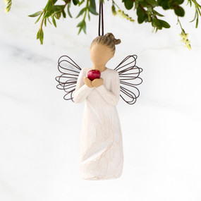 Front view of figure in cream dress with wire wings holding large red apple in hands, ornament hook on head