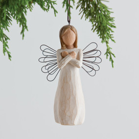 Small girl figurine wearing white dress holding arms across her chest, black wire wings - background is white with green branches