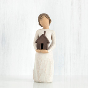 Faceless girl figurine facing forward wearing white dress, holding brown house figurine in her arms