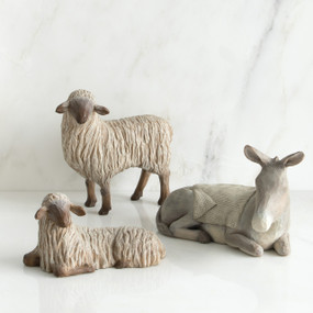 Two white lamb figurines next to grey donkey figurine with white blanket on its back