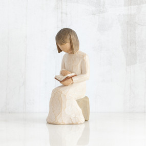 Young faceless girl figurine in white sitting on rock reading an open book
