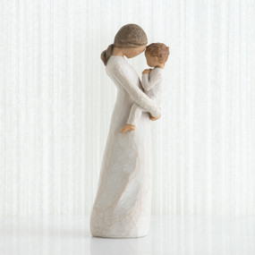 Side view of faceless mom figurine wearing white dress holding child in white outfit in her arms