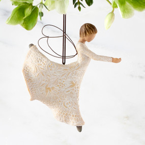 Right view of figure in cream dress carved with natural patterns in ballet pose with hands out and leg up behind her, wire wings on back and ornament hook on head