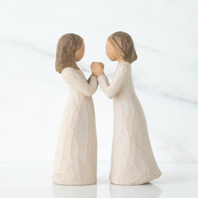Two brunette girl figurines in white dresses holding hands facing one another