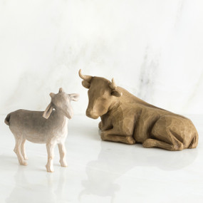 Brown cow figurine laying next to white goat figurine standing up