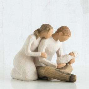 Faceless woman figurine in white dress leaning on faceless man figurine holding baby in his lap