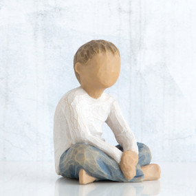 Small little boy figurine sitting down faceless, wearing white shirt and blue jeans