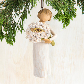 Close view of brunette girl figurine in white dress ornament holding white flower bouqet that says '2019' on it