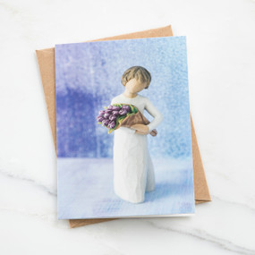 Front close view of blue card with brunette girl figurine in white dress holding purple flower bouqet