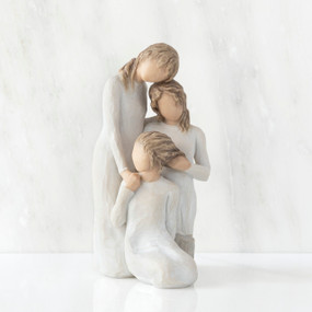 Front view, figurine of three females in cream dresses: one standing with arm around kneeling female, and holding hand of seated female