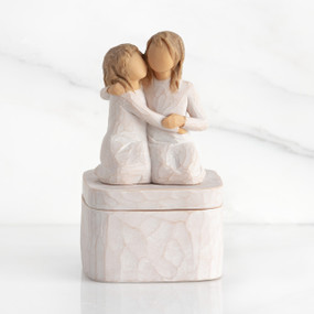 Square resin box, two 3-D figures kneeling atop lid, in cream dresses, hugging each other