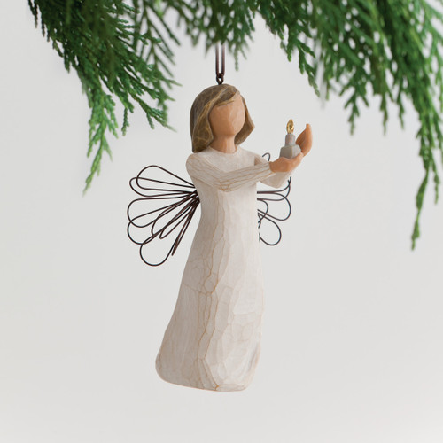 Faceless woman figurine in white dress with black angel wire wings holding candle - background is white with green tree branches