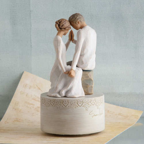 Faceless couple figurines sitting down holding hands in all white sitting on round white pedestal with music sheet and blue background