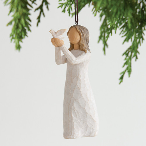 Hanging white faceless figurine girl ornament holding white dove - background is blurred green branches