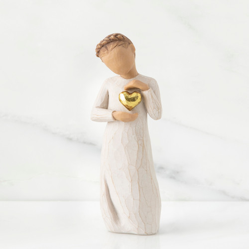 Small girl figurine wearing white dress holding up gold heart pendant