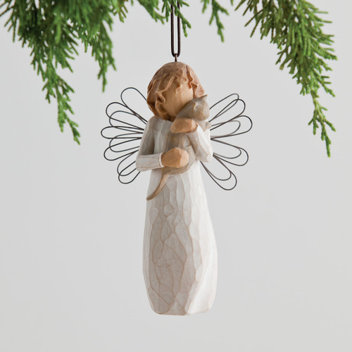 Faceless angel figurine ornament wearing white dress and holding grey cat - she has black wire wings - background is white with green branches