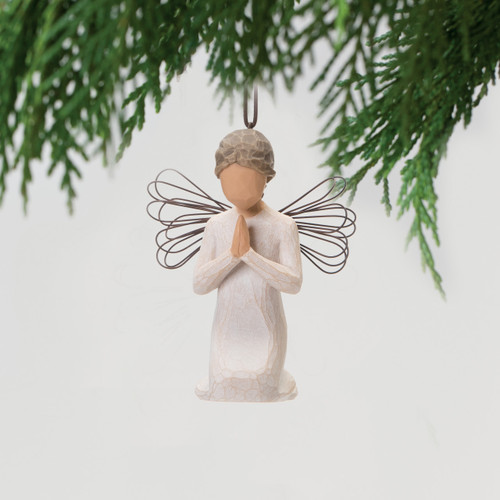 Small faceless angel wearing white dress and wire wings - hands are folded in prayer - background is white with green branches