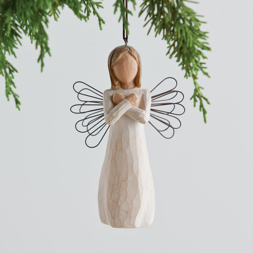 Small girl figurine wearing white dress holding arms across her chest, black wire wings - background is white with green branches