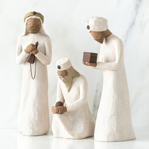 Set of three wiseman figurines -two are standing - far right one standing is holding brown box - one is sitting in the middle holding a rock