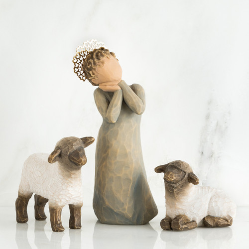 Angel faceless figurine wearing grey dress with hands on her face in between two white lamb figurines