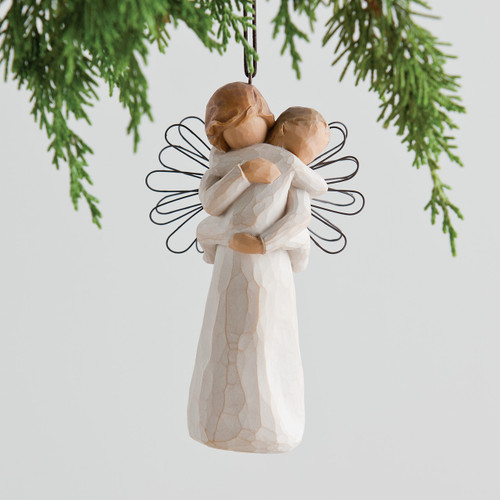 Faceless woman figurine hanging ornament holding baby to her chest - green branches in the background