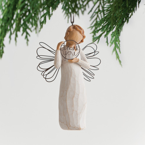 Faceless young girl figurine ornament in white holding up 'thank you' sign in black letters - background is hanging green branches