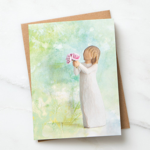 Notecard with blue and green background and figurine holding pink flowers sits on top of a brown envelope