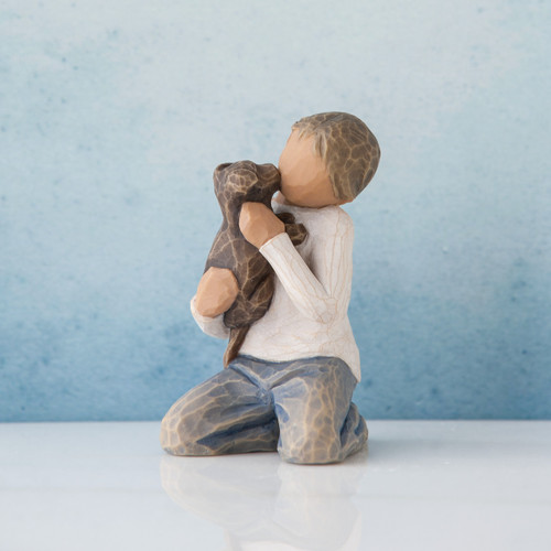Young faceless boy figurine wearing white shirt and blue jeans sitting holding brown puppy - background is blue