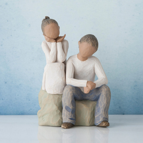 Young girl faceless figurine sitting on rock next to young faceless boy figurine wearing white shirt and blue jeans