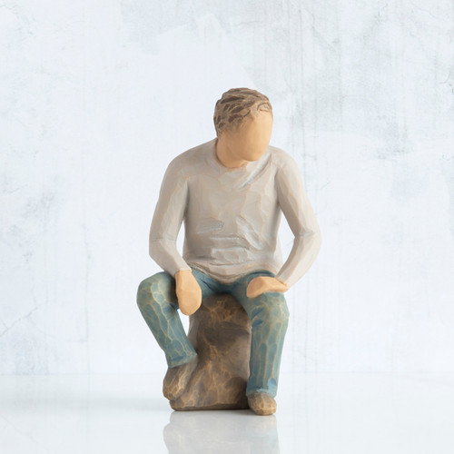 Front view, adult male figure in light gray shirt and blue jeans, seated on gray rock