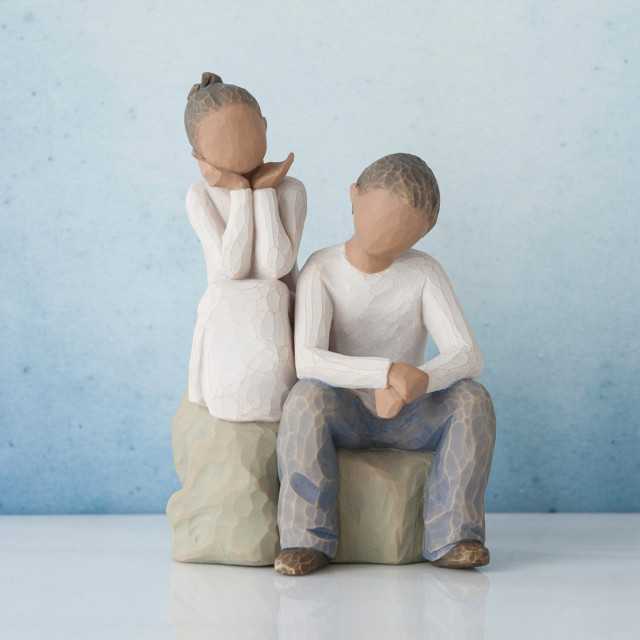 Young girl faceless figurine sitting on rock next to young faceless boy figurine wearing white shirt and blue jeans