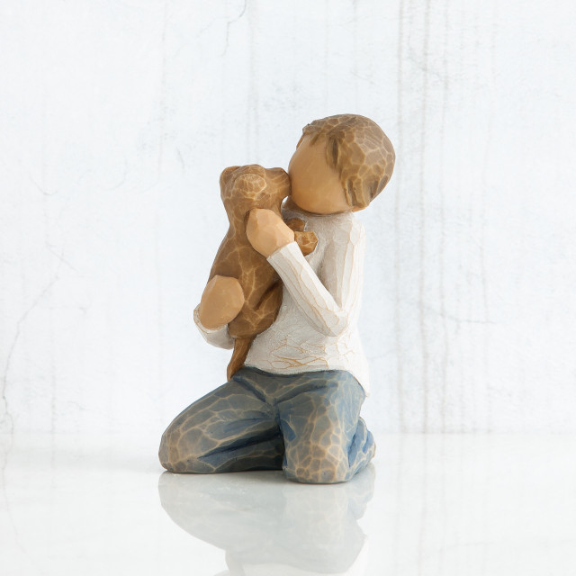Front view of boy with iight brown hair wearing white shirt and jeans and holding a light brown puppy as it licks his face.