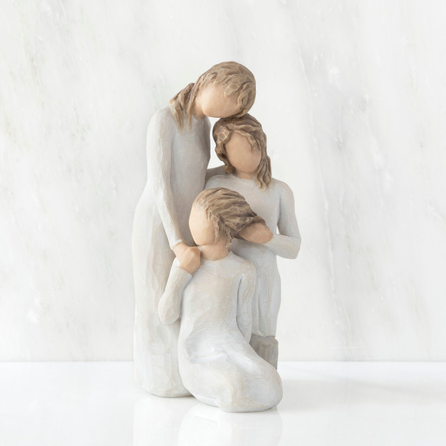 Front view, figurine of three females in cream dresses: one standing with arm around kneeling female, and holding hand of seated female
