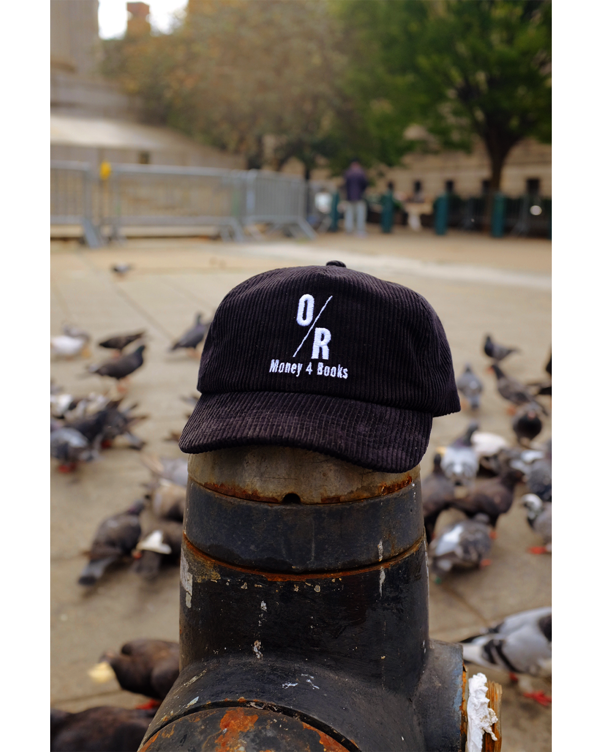 A black corduroy hat with the OR Books logo and 'Money 4 Books' written under it, placed on a fire hydrant
