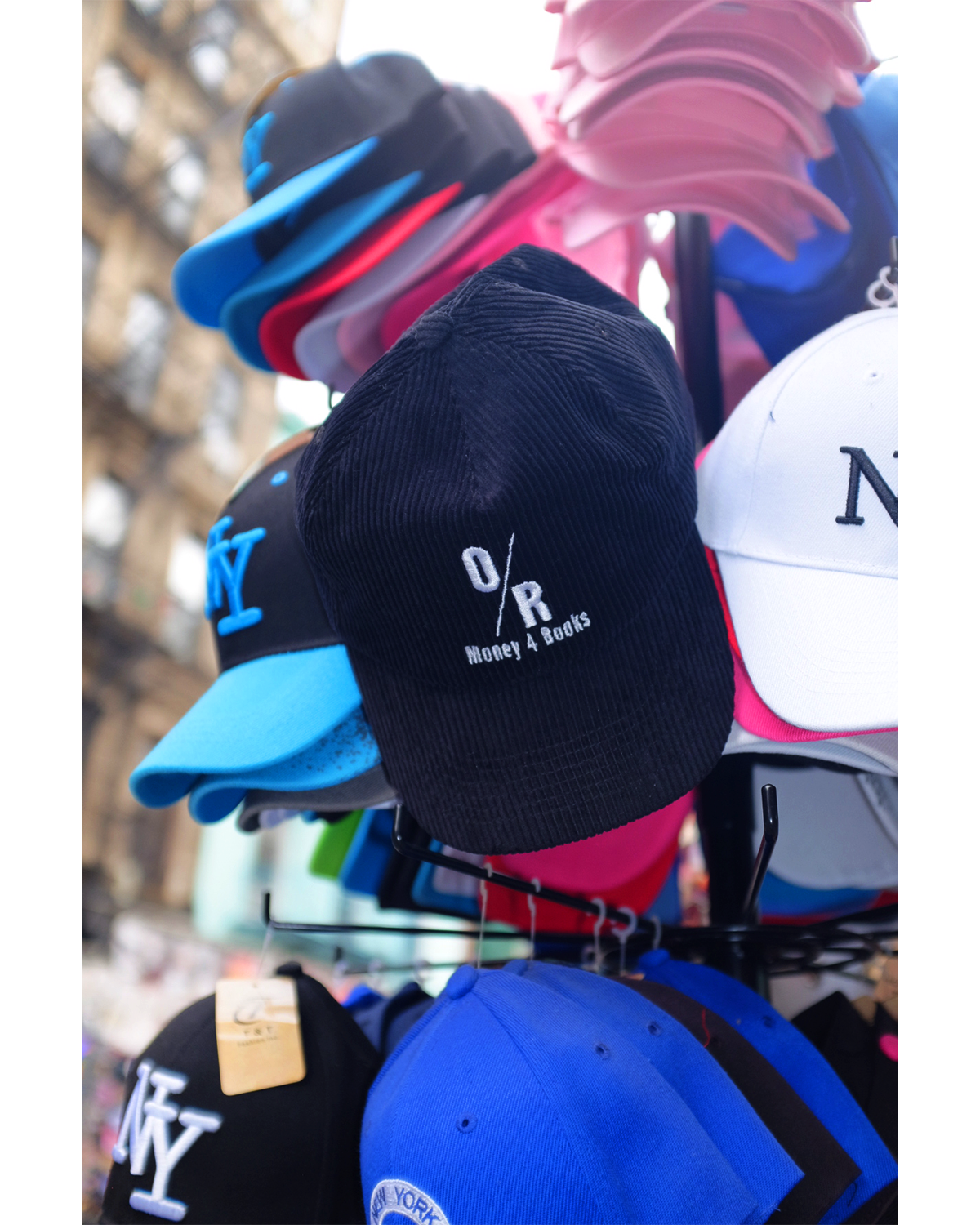 A black corduroy hat with the OR Books logo and 'Money 4 Books' written under it, placed on a fire hydrant