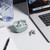 Grey wireless earbuds with open charging case, shown next to laptop on desk