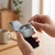 Grey wireless earbuds charging in open case, held above smartphone