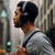 Black over-ear headphones worn outdoors with grey shirt and backpack strap visible