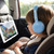 Child wearing blue headphones watching cartoon on tablet in car seat