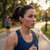 Woman jogging in park wearing blue wireless earbud and navy sports top