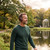 Man in green jumper wearing brown wireless headphones outdoors by a lake