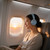 Woman wearing blue wireless headphones sitting by airplane window at sunset