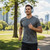 Man jogging in park wearing grey sports t-shirt, black shorts and blue headphones
