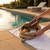 Poolside scene: tan backpack with sunglasses, book, sunscreen and portable speaker on towel