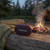 Portable red Bluetooth speaker on log by campfire, outdoor camping setting