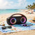 Portable black Bluetooth speaker with colourful lights on a beach towel