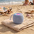 Blue portable Bluetooth speaker on towel at the beach, ideal for outdoor use
