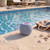 Blue portable Bluetooth speaker by poolside with beach bag and shells, summer outdoor setting
