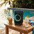 Black portable speaker with LED ring, shown on table by pool with tropical drinks