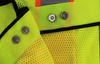 Durable snap-button attachment on reflective safety vest with reinforced stitching for industrial safety wear and high-visibility uniforms.